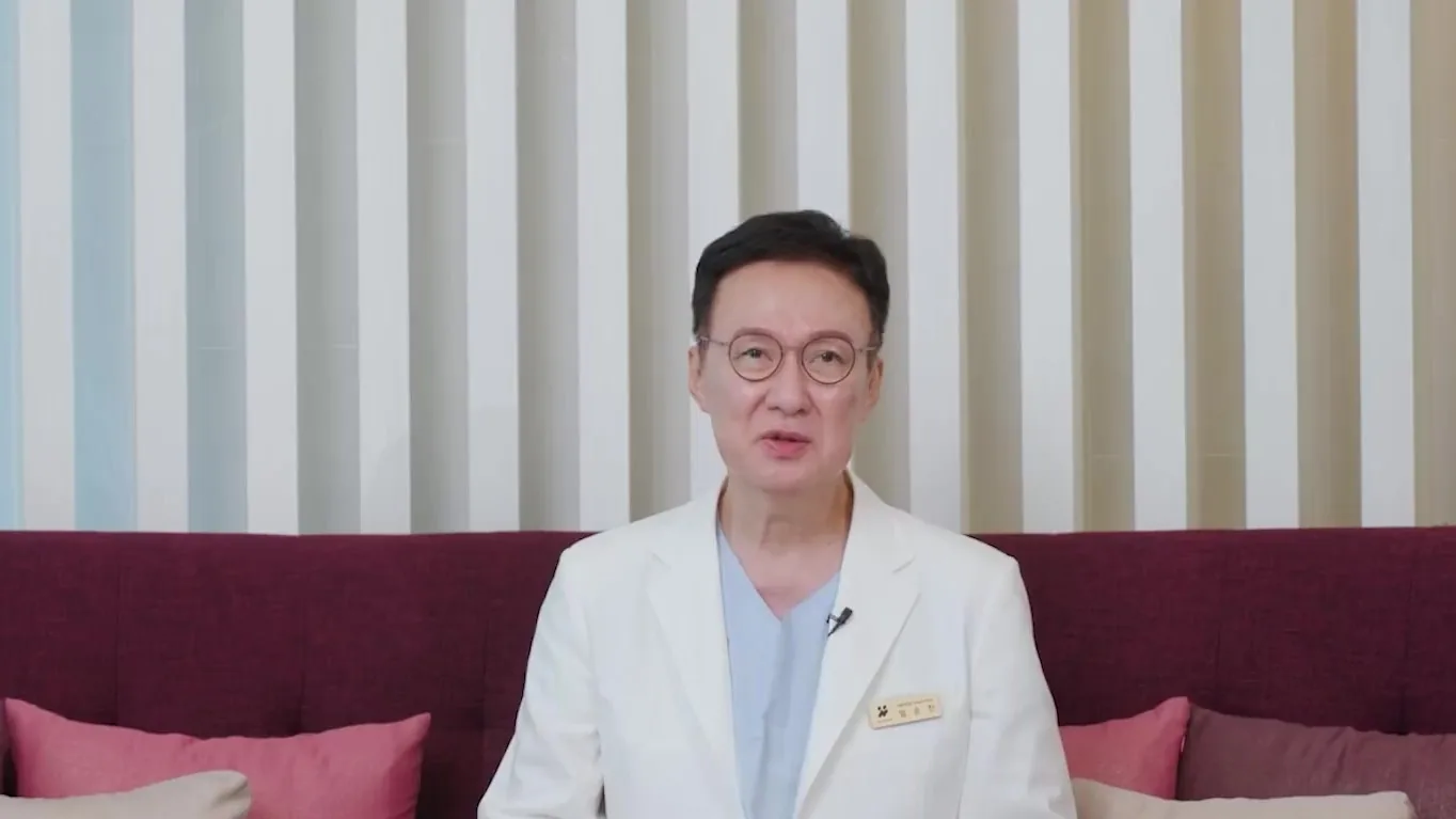 흰 가운을 입은 의사가 소파에 앉아 설명하는 모습