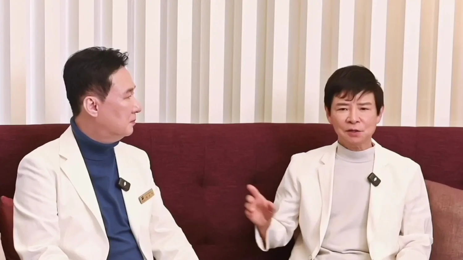 흰 가운 차림 의사 두 명이 소파에서 마주 보며 대화하는 모습